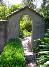 A stucco archway with gable Spanish tile roof and garden wall at the Casa del Herrero estate in Montecito CA