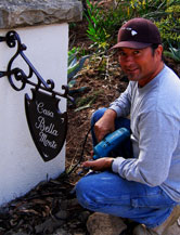Young man installing a Spanish style iron sign on plaster driveway column in Santa Barbara, California